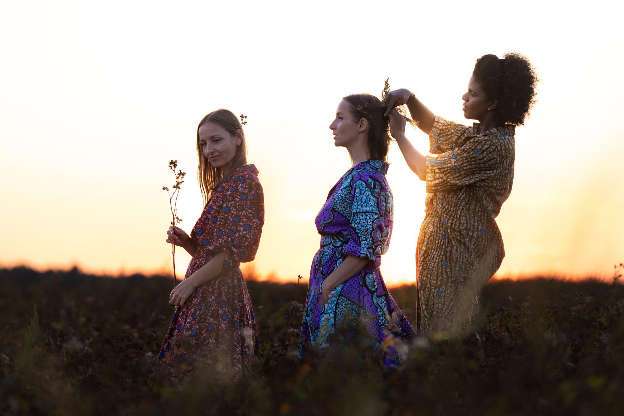 Three women in African print dresses in a field at sunset